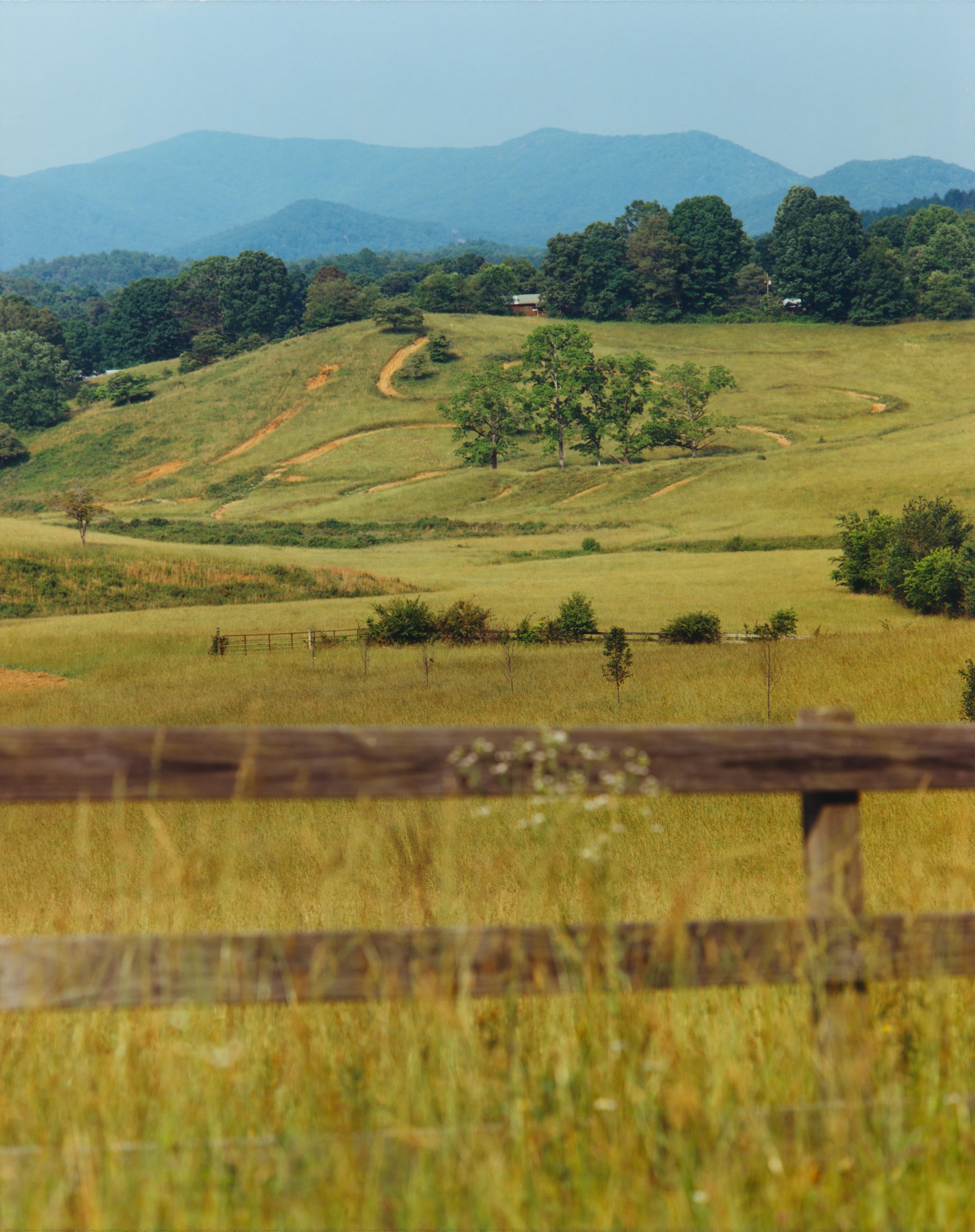 Rolling green hills with a wooden fence in the foreground and mountains in the distance as seen from Hwy. 60 in Georgia.