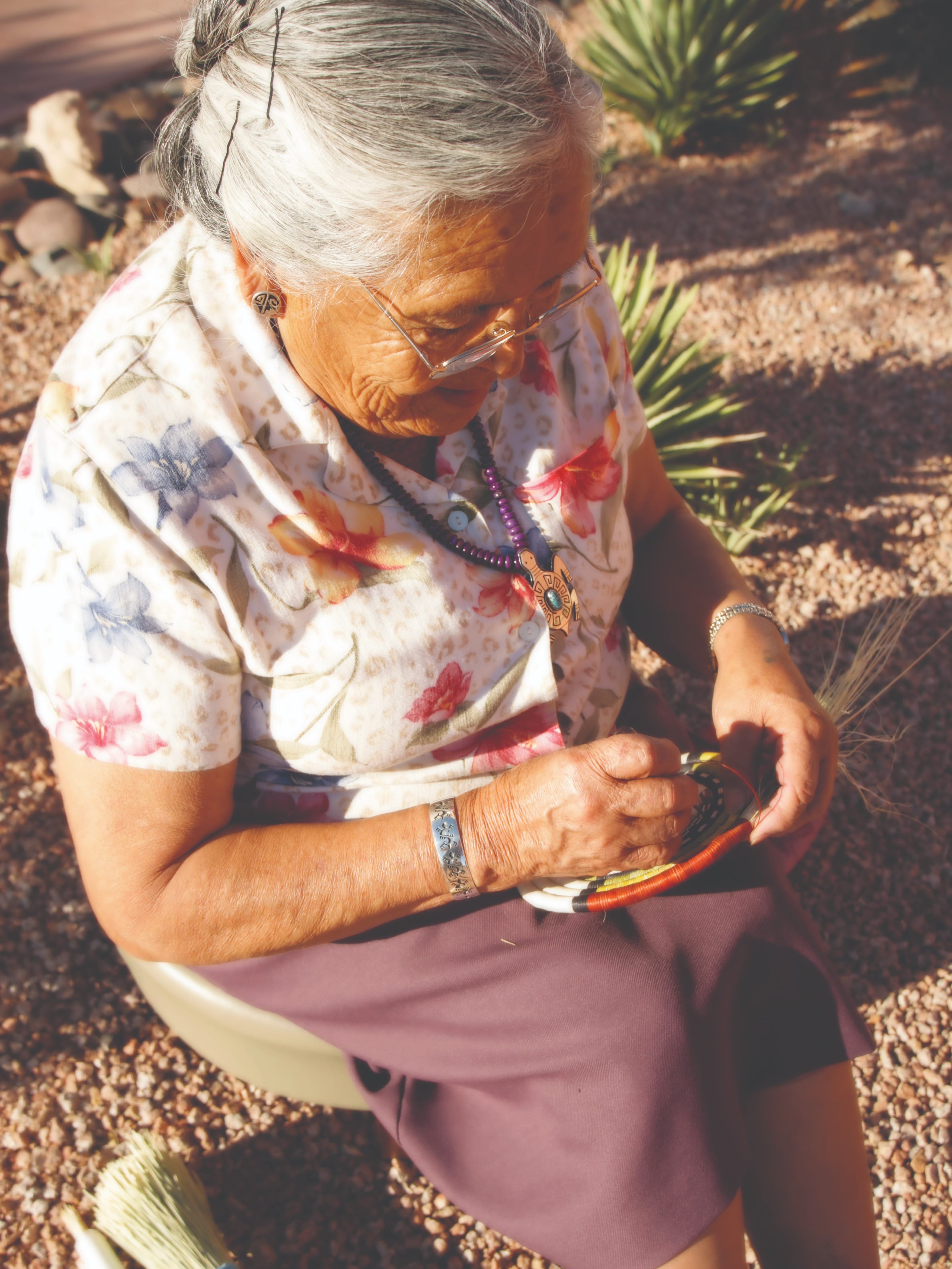 A woman sitting down outside weaving a basket
